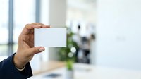 Businessman holding blank white business card in modern office environment with blurred background, suitable for corporate branding and marketing materials.