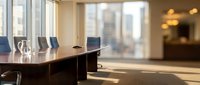 Modern corporate boardroom with conference table and chairs overlooking city skyline through large windows for business meetings and presentations.