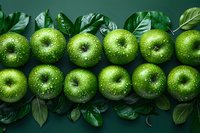 Fresh green apples with water drops arranged in rows on dark green background with scattered leaves, creating minimalist composition for healthy eating concept.