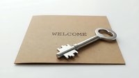 Vintage silver key resting on a kraft paper welcome card, symbolizing new home ownership, hospitality, and real estate concepts.