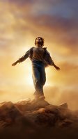 Young man standing on mountain peak with arms spread wide against dramatic sunset sky, expressing freedom and achievement in spiritual pose.