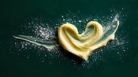 Golden heart-shaped pasta with flour explosion on dark green background for culinary design and cooking concepts.