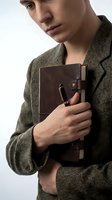 Young man, Caucasian ethnicity, wearing olive-green cardigan, holding brown leather portfolio with pen, studio portrait against white background for business and professional use.