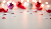 Romantic blurred background with warm bokeh lights and scattered rose petals on white surface for Valentine's Day celebration and love themes.