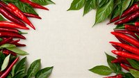 Fresh red hot chili peppers and green bay leaves creating frame border on white linen textile background with copy space for text in center.