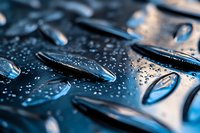 Water droplets on dark metallic surface create abstract pattern with dramatic lighting and reflections, showing surface tension and hydrophobic effect.