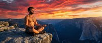 Shirtless athletic man meditating in lotus position on mountain cliff edge during dramatic sunset with orange and red sky over canyon landscape for wellness.