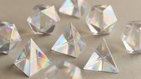 Crystal clear glass prisms and geometric shapes creating rainbow light reflections on neutral background for optical physics education and design projects.