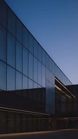 Modern glass facade of contemporary office building at dusk with illuminated interior spaces, reflecting clear evening sky. Suitable for corporate, architecture, and commercial design projects.