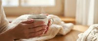 Woman hands holding warm coffee mug in cozy morning light by window. Relaxing home atmosphere with soft natural lighting for lifestyle content.