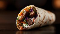 Grilled beef shawarma wrap with fresh vegetables, rice, and purple cabbage in tortilla flatbread on dark wooden background, close up view of middle eastern food.