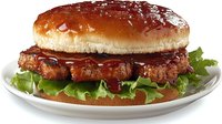 Juicy grilled burger with crispy bacon, fresh lettuce and barbecue sauce on glossy bun served on white ceramic plate. For restaurant menu and food advertising.