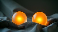 Glowing orange spheres nestled in soft gray fabric folds create mysterious ambient lighting effect against dark background, evoking calm meditative atmosphere.