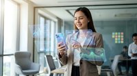 Professional Asian businesswoman using smartphone with holographic data visualization interface in modern office environment for digital technology presentations.