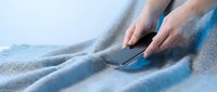 Woman's hands placing a smartphone on a soft blue knitted blanket, cozy home atmosphere, comfort and relaxation concept.