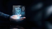 Businessman hand holding glowing holographic device displaying secure data protection interface with digital lock icons and shield symbol on dark background.