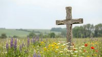 Wooden cross stands in wildflower meadow with purple lupines, yellow daisies and red poppies blooming in peaceful countryside setting for memorial concepts.