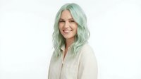 Young Caucasian woman with mint green wavy hair smiling warmly in cream blazer on white background isolated for professional headshot and business portrait.