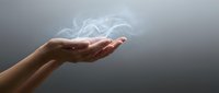 Hand holding glowing light particles and smoke against gray background, representing energy, magic, innovation, and digital transformation for business and technology concepts.