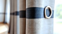 Modern curtain with metallic grommet and navy blue stripe pattern creates elegant window treatment. Soft natural lighting adds depth to textured fabric detail.