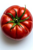 Fresh ripe red heirloom tomato with green stem and natural texture on white background, top view macro photography for food and cooking concepts.