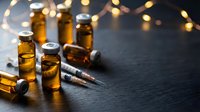Amber glass medical vials and syringes on dark surface with warm bokeh lights creating pharmaceutical research atmosphere for healthcare concepts.