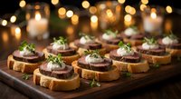 Elegant appetizer canapes with meat pate and cream cheese on toasted bread, garnished with fresh herbs on wooden board with warm bokeh lights background.