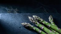 Fresh green asparagus spears on dark slate background for healthy cooking and gourmet cuisine preparation.