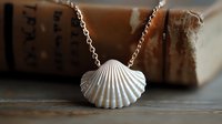Silver seashell pendant necklace on delicate chain against vintage book background, macro jewelry photography with soft natural lighting and shallow depth of field.