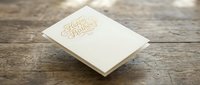 Elegant cream-colored wedding invitation with gold foil lettering on rustic wooden background for luxury stationery and event planning designs.