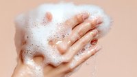 Female hands covered in white soap foam and bubbles against pink background, showing personal hygiene and cleanliness concept for skincare and washing.