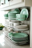 Organized kitchen cabinet with mint green dinnerware set on chrome wire shelving racks displaying plates bowls and cups in modern home interior storage solution.