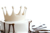White fondant crown on top of round cake with chocolate drip effect against light background, modern minimalist dessert styling for celebrations.