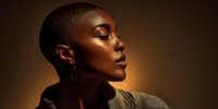 Profile of African American woman with short hair and hoop earrings illuminated by warm golden light against dark brown background.