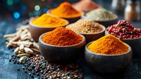 Vibrant aromatic spices and seasonings in rustic bowls on dark background with turmeric, paprika, black peppercorns and dried chili peppers for cooking.