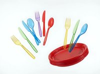Colorful disposable plastic cutlery set with forks, knives, and spoons in red, blue, yellow, and green arranged around red plates, isolated on white background for party and event design use.