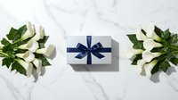 White gift box with navy blue ribbon surrounded by fresh white tulips on elegant marble surface for special occasions and celebrations.