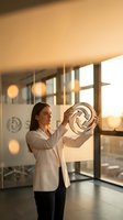 Professional businesswoman examining circular architectural model in modern office during golden hour sunset lighting for corporate design presentations.