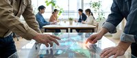 Business professionals analyzing holographic data visualization on interactive table during corporate meeting in modern office environment.