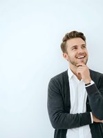 Young Caucasian man with styled blonde hair wearing dark cardigan over white shirt, smiling thoughtfully with hand to chin against white background for business and lifestyle use.