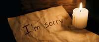 Handwritten I'm sorry note on crumpled parchment paper beside a glowing candle in dark moody setting, evoking regret and apology.