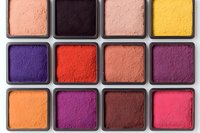Colorful makeup eyeshadow palette with vibrant pressed powder squares in purple, pink, orange, yellow and coral shades arranged in rows on white background.
