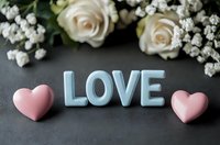 Romantic composition with blue LOVE text and pink hearts on dark background, decorated with white roses and baby's breath flowers for wedding or valentine design.