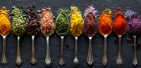 Colorful aromatic spices and herbs in vintage silver spoons on dark stone background, panoramic food composition for cooking and seasoning.