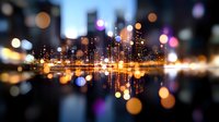 Modern city skyline reflected in water at night with glowing bokeh lights creating dreamy urban landscape with colorful defocused circles in foreground.