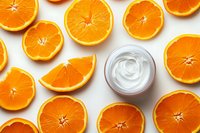 Fresh orange slices arranged around white moisturizing cream jar on white background, flat lay composition for cosmetic and skincare product photography.