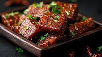 Glazed pork belly chunks with caramelized coating and fresh herbs served on dark wooden plate. Asian cuisine meat dish with sweet and savory marinade.