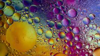 Vibrant oil and water abstract macro photography with colorful bubbles in yellow, purple, and blue creating psychedelic patterns against dark background.