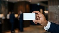Businessman holding blank white business card in hand at corporate event with blurred office background, suitable for branding and professional networking materials.
