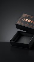 Elegant black gift box with copper moon phases and botanical design elements on dark background for luxury packaging and mystical branding projects.